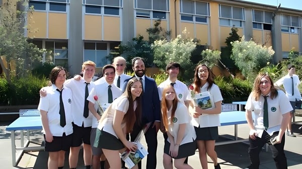 Un grupo de estudiantes está frente a un edificio con grandes ventanas en el campus de The Forest High School.