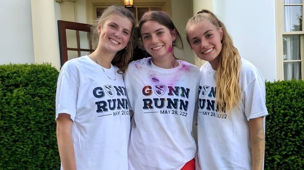 Tres estudiantes de la The Frederick Gunn School posan juntas frente a un edificio con un seto verde.