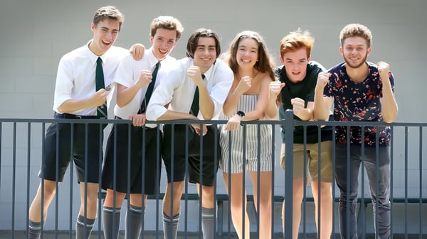 Un grupo de estudiantes de la The Gap State High School está frente a un fondo gris y sonríe a la cámara.