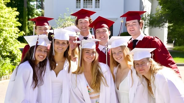 Graduadas y graduados de The Governor's Academy en togas blancas y birretes rojos están frente a un edificio con un entorno verde.