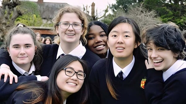 Un grupo de estudiantes sonrientes de The High School está reunido al aire libre frente a árboles y edificios.