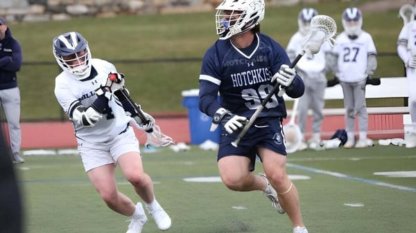 Dos jugadores de lacrosse de The Hotchkiss School corren en el campo deportivo mientras otros jugadores son visibles en el fondo.