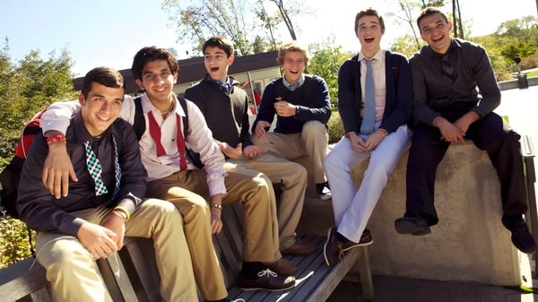 Un grupo de jóvenes en ropa formal sentados en un muro de piedra en el campus de The Hun School of Princeton.