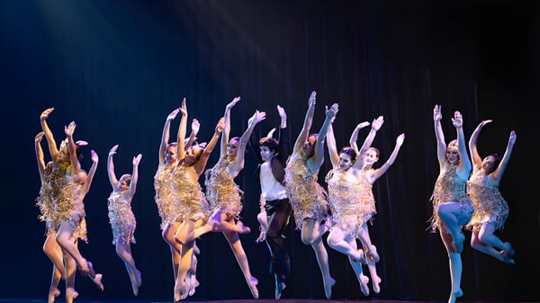Un grupo de estudiantes de The King's Academy realiza una actuación de baile en brillantes disfraces en un escenario oscuro.