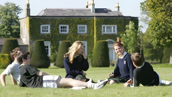 Un grupo de estudiantes está sentado en la hierba frente al edificio histórico con torre en el campus de The Kings Hospital.