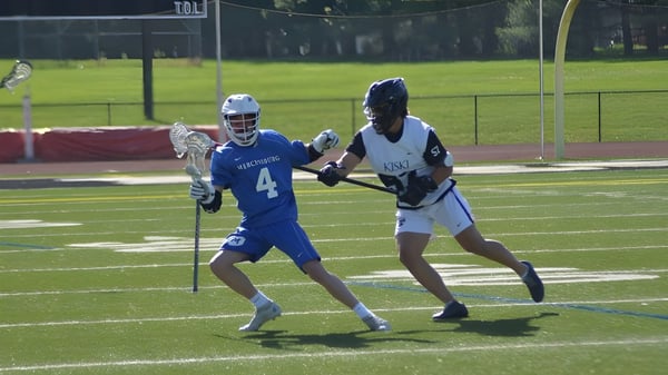 Dos jugadoras en uniforme de lacrosse compiten entre sí en el campo de juego de The Kiski School.