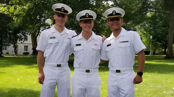 Tres personas en uniformes navales blancos están de pie sobre un césped con árboles de fondo en el campus de The Kiski School.