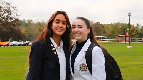 Dos estudiantes de The Knox School están sonriendo en un prado frente a un edificio.