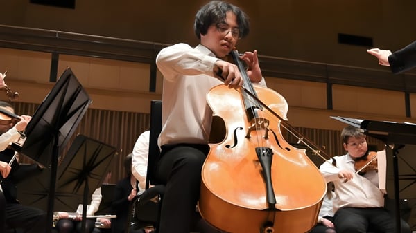 Un hombre toca el violonchelo en el escenario durante un concierto de The Leys School con otros músicos.