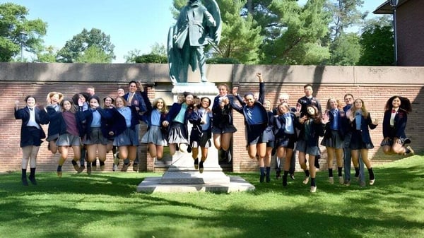 Un grupo de estudiantes de The Linsly School está frente a un monumento en el campus con árboles y edificios de fondo.
