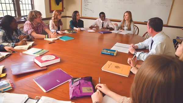 Un grupo de estudiantes y un docente de The Masters School trabajan juntos en una gran mesa de madera en el aula.