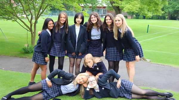 Un grupo de estudiantes de The Mount School York está de pie en un prado frente a unos árboles.