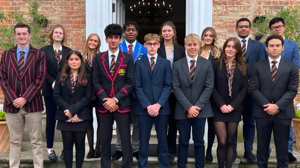 Un grupo de estudiantes de The Oratory School está en ropa formal frente a un edificio de ladrillo con un candelabro en la entrada.