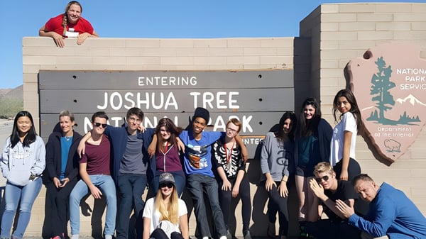 Estudiantes de The Orme School están frente al cartel de entrada del Parque Nacional Joshua Tree en el paisaje desértico.
