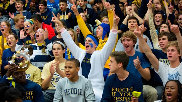 Muchos estudiantes de The Peddie School animan y levantan los brazos en un evento deportivo.
