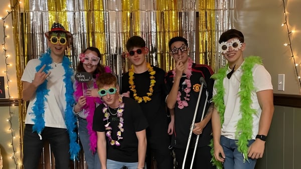 Un grupo de estudiantes de The Phelps School posan frente a un fondo de cortinas doradas y plateadas en coloridos trajes festivos.