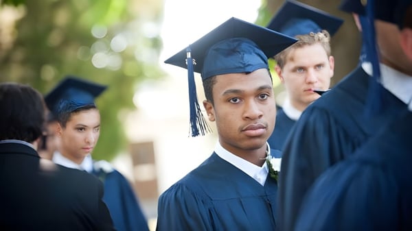 Un grupo de graduados de The Phelps School está de pie en togas negras al aire libre frente a árboles.