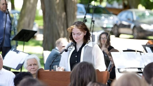 Una mujer con cabello rizado da un discurso en el podio frente a un grupo de personas en el campus de The Putney School.