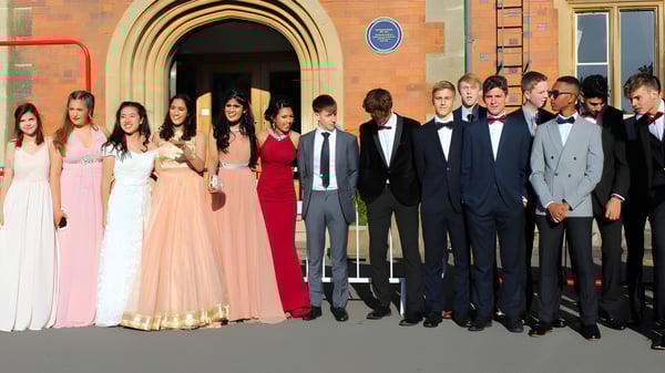 Un grupo de personas vestidas formalmente posan frente a un arco decorado en el campus de The Royal School Wolverhampton.