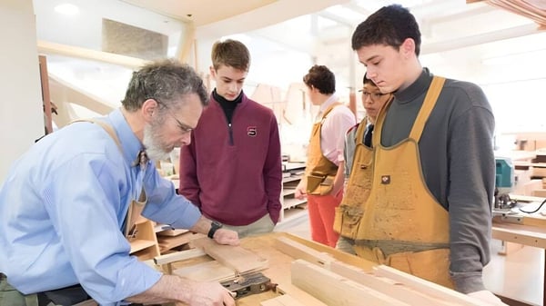 Un grupo de estudiantes y un hombre mayor trabajan juntos en una mesa de trabajo en el campus de The Salisbury School.
