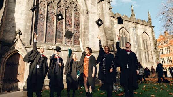 Un grupo de graduadas y graduados del The Sheffield College está frente a una catedral gótica en otoño.