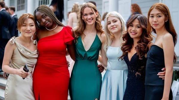 Un grupo de mujeres en vestidos coloridos en una calle frente a edificios en el campus de The Stony Brook School.