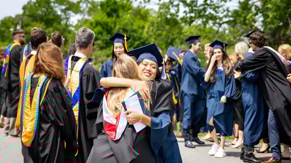 Un grupo de graduadas y graduados de la The Storm King School está al aire libre frente a árboles en vestimenta académica.
