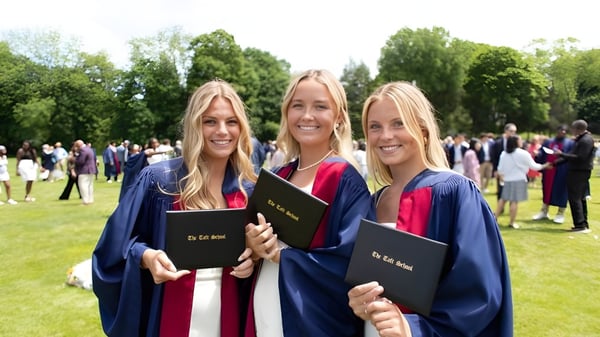 Tres estudiantes de The Taft School están al aire libre con birretes de graduación y diplomas juntos.