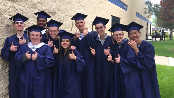 Un grupo de graduados de The Vanguard School se encuentra frente a un edificio de ladrillo y muestra el pulgar hacia arriba.
