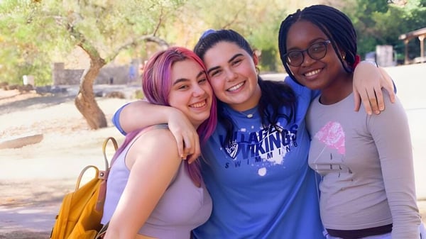 Tres alumnas se abrazan y sonríen en el área exterior de The Village School.