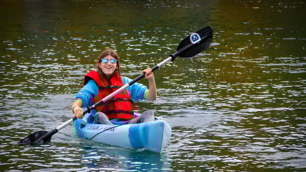Una persona con un chaleco salvavidas rojo rema en un kayak azul sobre el agua en el terreno de The Village School.