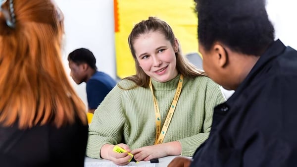 Una mujer con un suéter verde está conversando con dos personas en el campus de The Wren School.