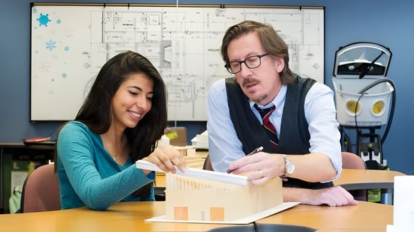 Una joven y un hombre mayor están sentados a una mesa y mantienen una conversación en el campus de The Academy MiraCosta.