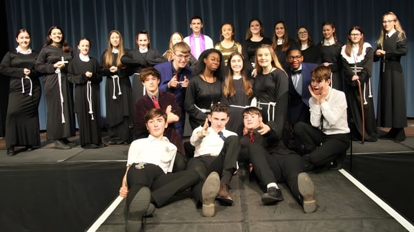 Un grupo de estudiantes de la Theale Green School posan juntos en un escenario frente a una cortina oscura.