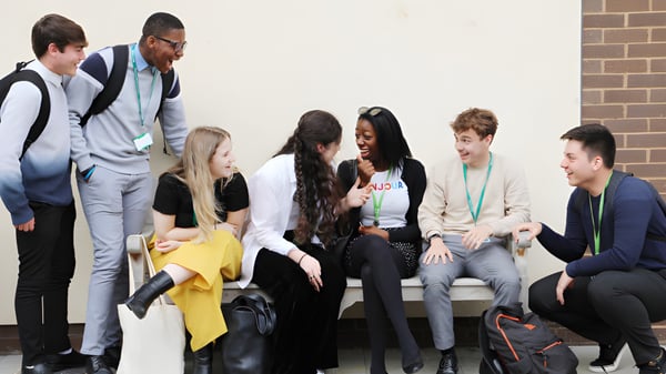 Un grupo de estudiantes de la Theale Green School está sentado junto en un aula con pared de ladrillo y conversan.
