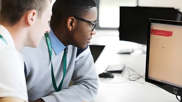 Dos personas en una computadora de oficina en el campus de la Theale Green School se concentran en la pantalla.