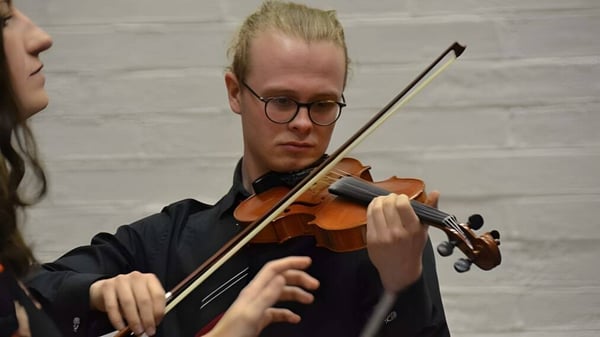 Un estudiante de The High School toca concentrado el violonchelo frente a una pared de ladrillo blanco.