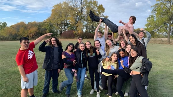 Un grupo de estudiantes de la Thomas A. Blakelock High School se reúne afuera en un área parecida a un parque con árboles y césped.