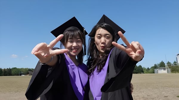 Dos graduadas de la Thornlea Secondary School están en un campo cubierto de hierba mostrando signos de paz con las manos.