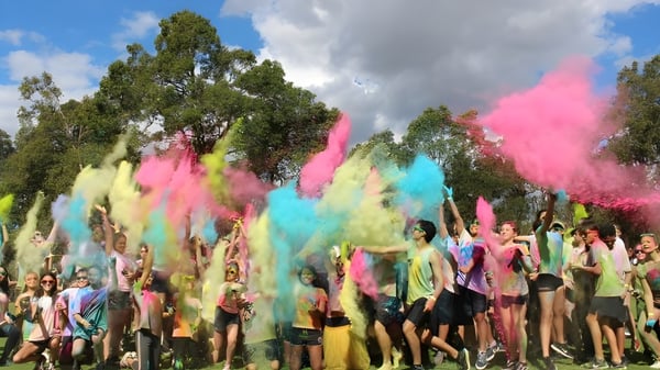 Estudiantes de la Thornlie Senior High School celebran al aire libre con polvo de colores bajo un cielo azul y vegetación verde.