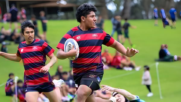 Dos jugadores de rugby con camisetas a rayas corren en el campo de la Thornlie Senior High School.