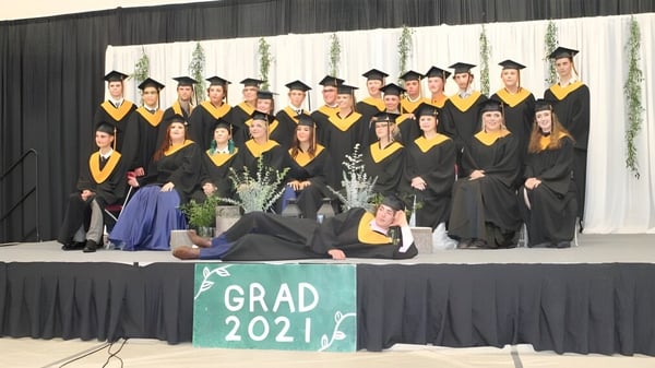 Graduados de la Thorsby Junior Senior High School posan en toga de graduación frente a un banner con la inscripción Grad 2021.