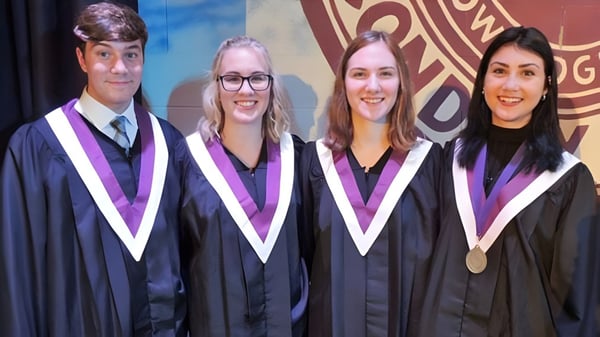 Cuatro alumnas y alumnos de la Thousand Islands Secondary School están en ropa de graduación frente a un fondo colorido con el logo de la universidad.