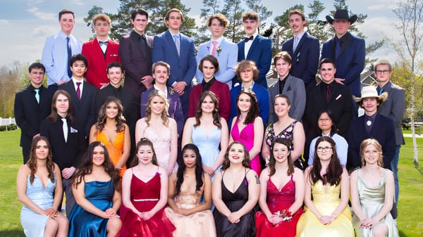 Estudiantes de la Three Hills School están juntos en ropa formal en un prado con árboles al fondo.
