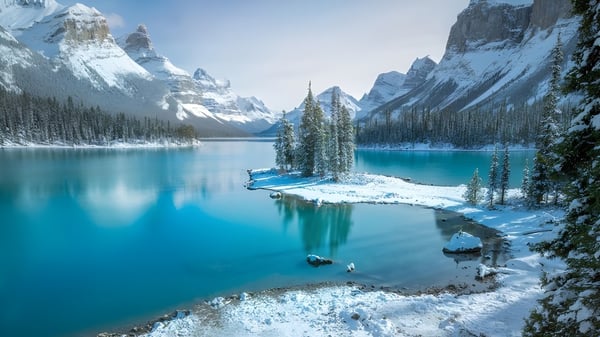 Paisaje nevado con lago turquesa e isla boscosa en las montañas cerca de la Three Hills School.
