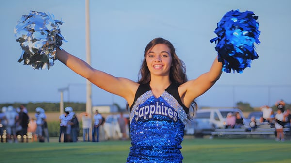 Una animadora de la Thunder Ridge High School está en el campo deportivo y saluda con pompones azules y plateados.