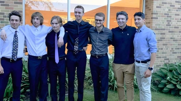 Un grupo de estudiantes está frente a un edificio de ladrillo con una pared naranja en el campus de la Tilbury District High School.