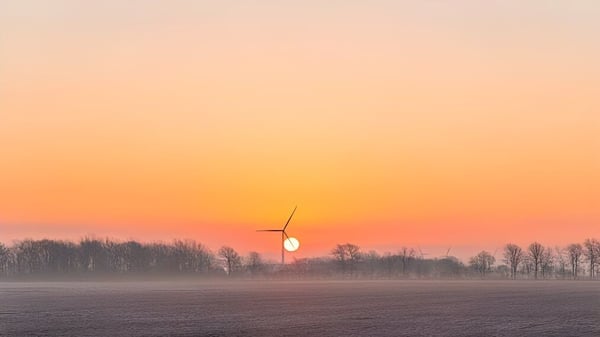Turbina eólica frente a un colorido atardecer sobre un campo neblinoso en los alrededores de la Tilbury District High School.