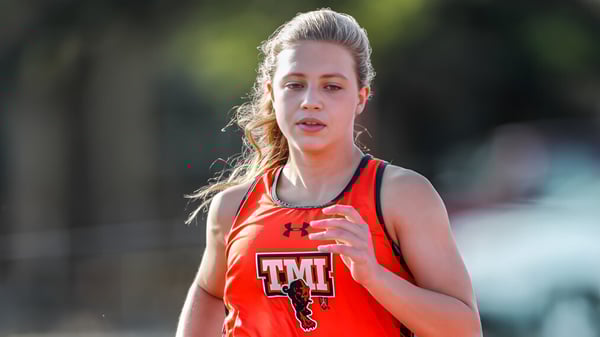 Una alumna de TMI Episcopal está en la camiseta deportiva roja al aire libre frente a un fondo borroso con árboles.