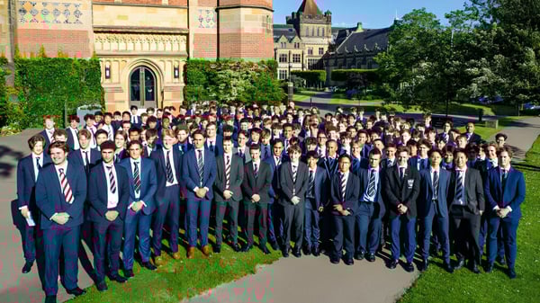 Un gran grupo de estudiantes vestidos formalmente se encuentra frente a un edificio histórico en el terreno de la Tonbridge School.